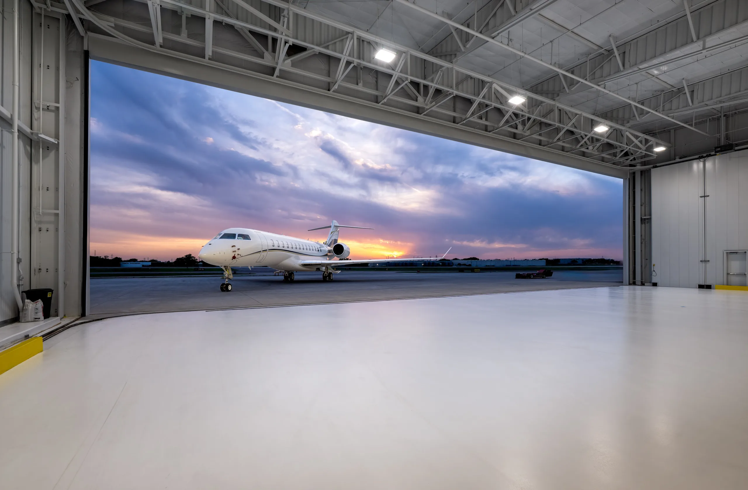 A long-range business jet waiting outside an open hangar at dusk